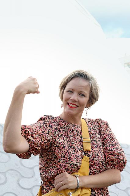 Pia i blommig klänning spänner upp armmuskeln.