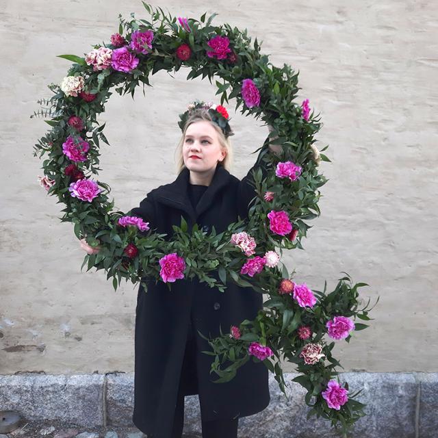 Emmi håller i en stor blomkrans formad som tecknet för kvinna.